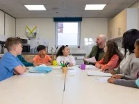 Ein Sozialassistent kümmert sich in einer Gemeinschaftsküche um eine Gruppe Kinder verschiedener ethnischer Herkunft. 