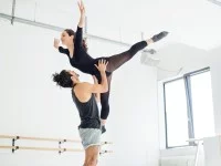 Eine Bühnentänzer hebt ein Bühnentänzerin im Proberaum mit seinen Händen hoch. 