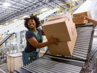 Eine Fachlageristin arbeitet in einem Logistikzentrum an einer Förderanlage für Kisten und Kartons.