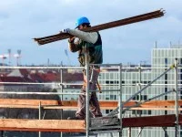 Ein Gerüstbauer transportiert Holzbretter für ein Gerüst auf einer Baustelle.
