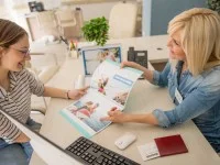 Eine Kauffrau für Tourismus und Freizeit berät im Reisebüro eine Kundin über Reiseziele am Meer.