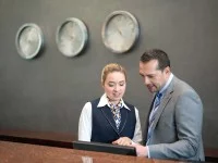 Ein Kaufmann für Hotelmanagement informiert sich bei seiner Kollegin am Empfang über die Reservierungen des Hotels, um den Personaleinsatz der nächsten Wochen besser planen zu können.