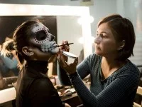 Eine Maskenbildnerin schminkt das Gesicht einer Frau mit einem Totenkopfmotiv.