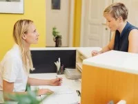 Eine Medizinische Fachangestellte spricht am Empfang einer Praxis mit einer Patientin.