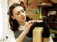 Eine Sattlerin näht in der Werkstatt an einer Tasche.