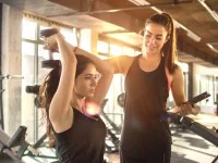 Eine Sportfachfrau leitet im Fitnessstudio eine Kundin beim Hanteltraining an.