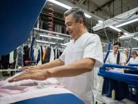 Ein Textilreiniger bügelt Kleidung mit einer Dampfbügelmaschine.