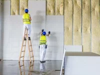 Zwei Trockenbaumonteure installieren Gipsplatten an einer mit Dämmmaterial versehenen Wand.