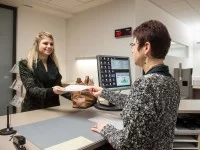 Eine Verwaltungsfachangestellte übergibt Unterlagen an eine Bürgerin.