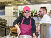 Eine Fachkraft Küche unterstützt den Koch eines Wirtshauses bei der Zubereitung der wohlschmeckenden Speisen.